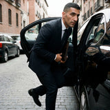 Usuario bajandose de un coche negro con un traje negro y una corbata de seda negra